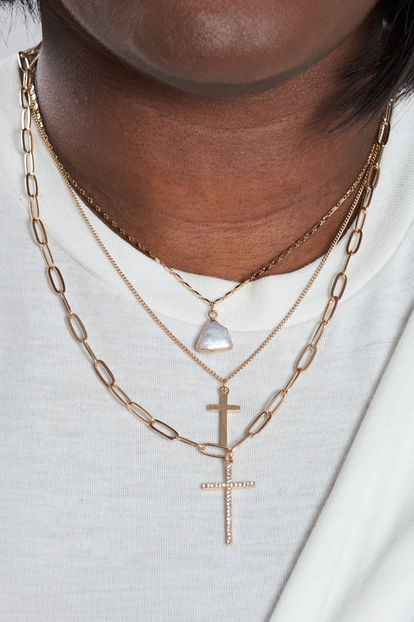Close-up of a person wearing gold necklaces with a cross pendant on a white background